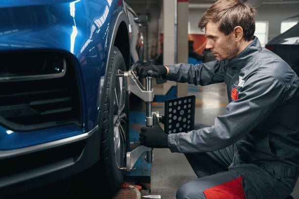 Mechanic in blue uniform aligning a car's tire in a garage, using equipment.