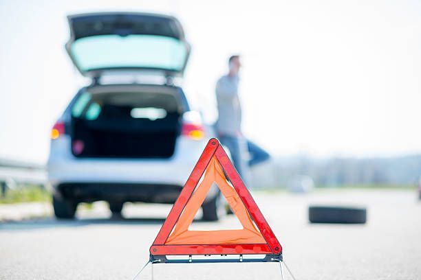 A man with a flat tire by his car, a warning triangle on the road.