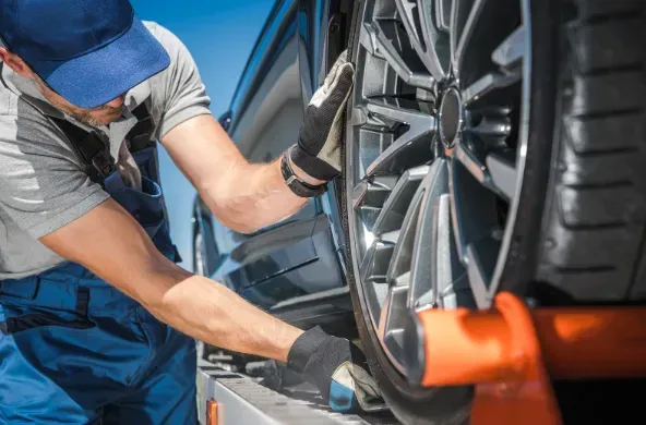 A tow truck operator securing a car wheel with orange straps.