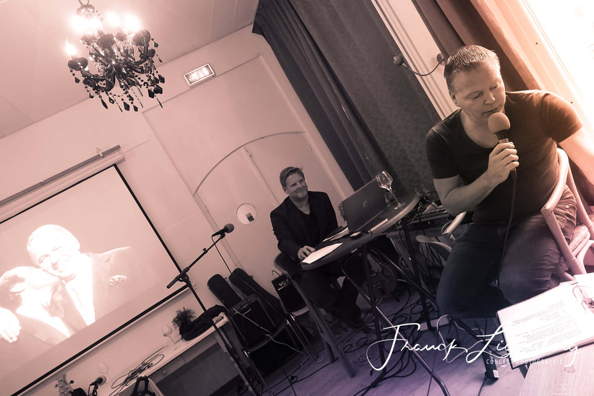 Een man zingt in een microfoon terwijl een andere man een toetsenbord bespeelt