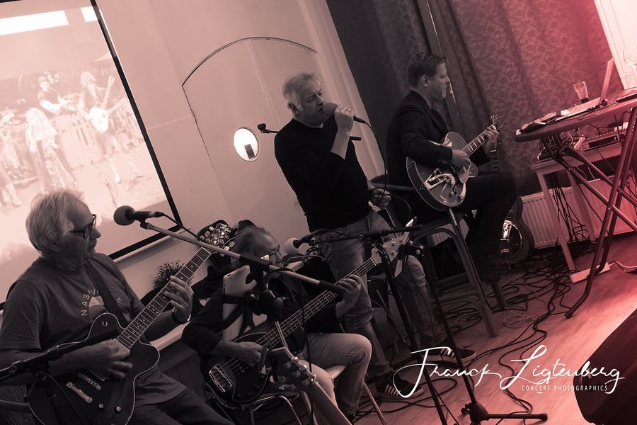 Een groep mannen speelt gitaar en zingt in microfoons in een kamer.