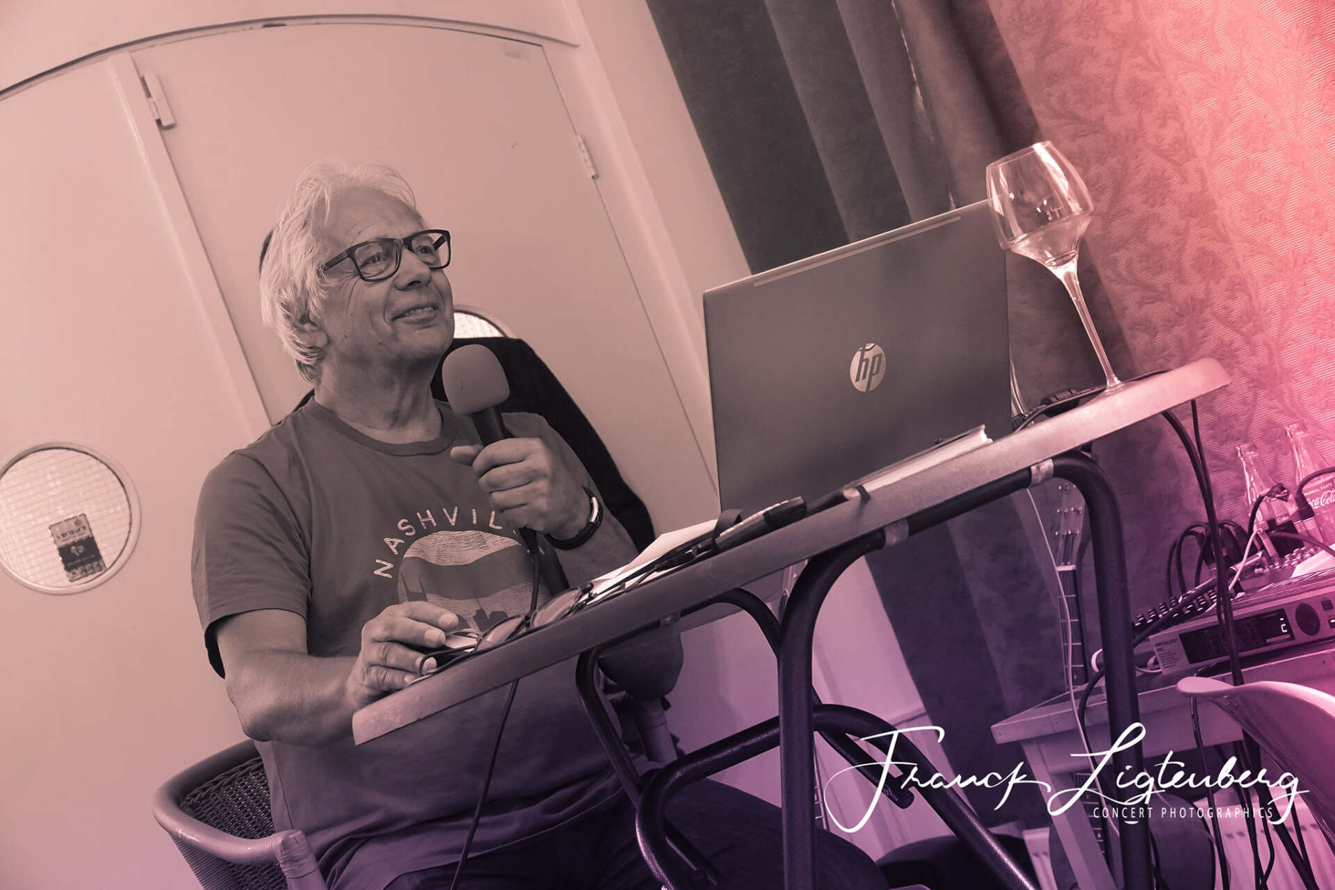 Een man zit aan een tafel met een laptop en een microfoon.