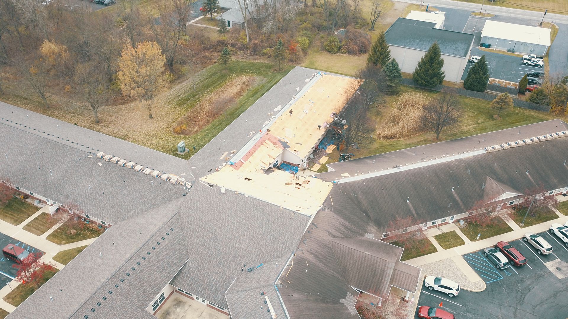 Aerial view of a commercial building roof under construction with workers and parked vehicles nearby.
