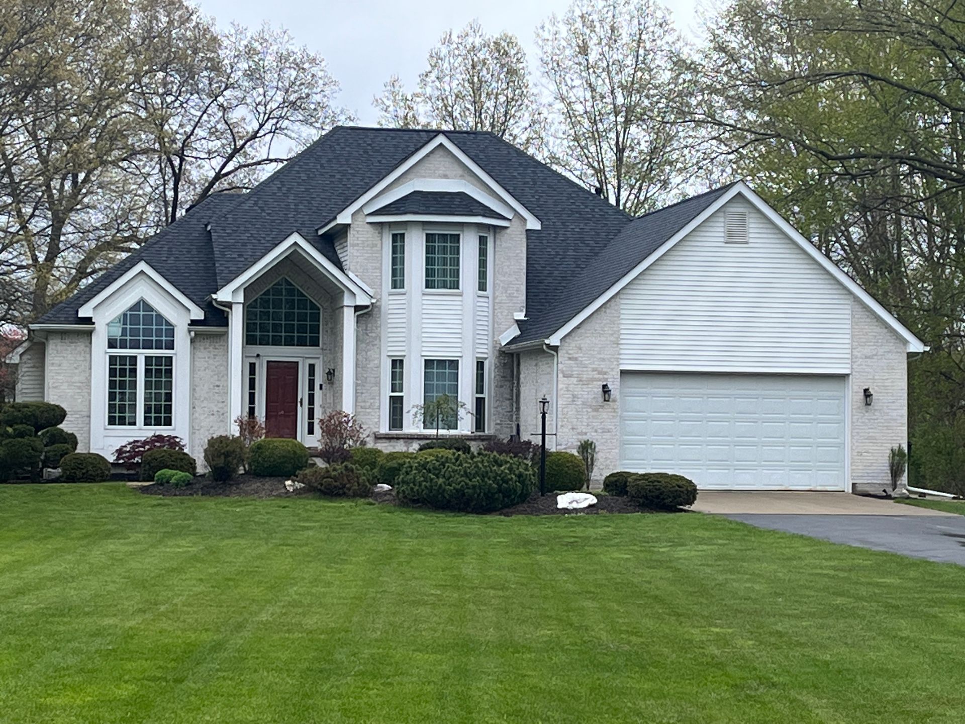 White brick house with dark roof, manicured lawn, and two-car garage.
