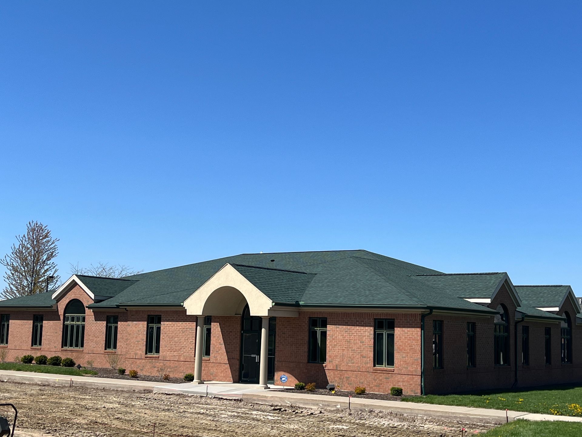 Brick commercial building with dark green roof under blue sky.