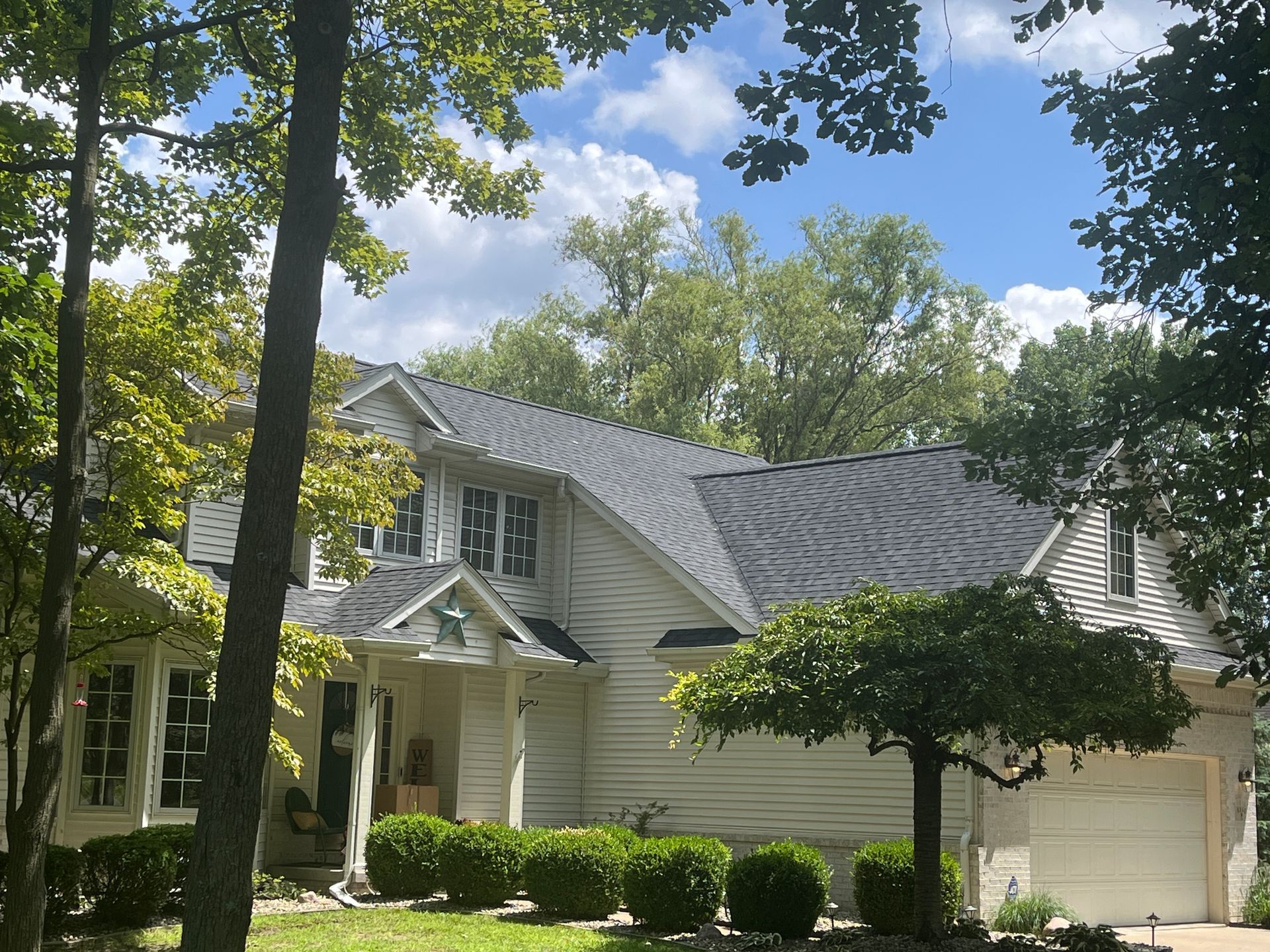 White house with unique roofline and garage, surrounded by trees under a partly cloudy sky.