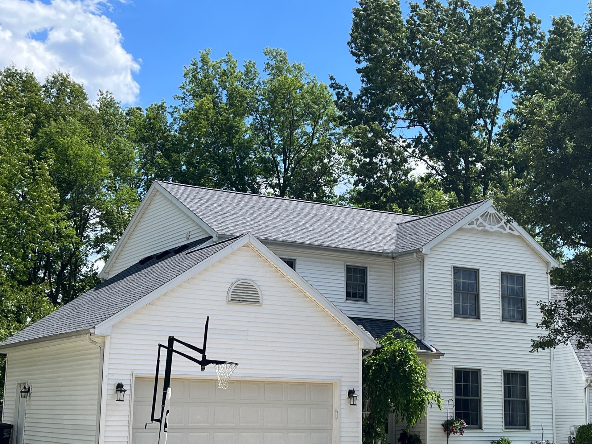 White two-story house with a grey roof and a basketball hoop in the driveway, blue sky in background.