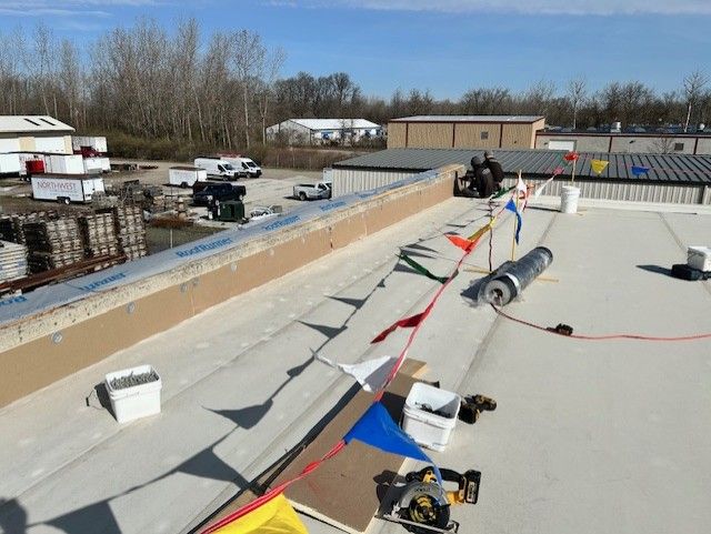 Construction workers on a flat roof install flashing, marked by safety flags. 