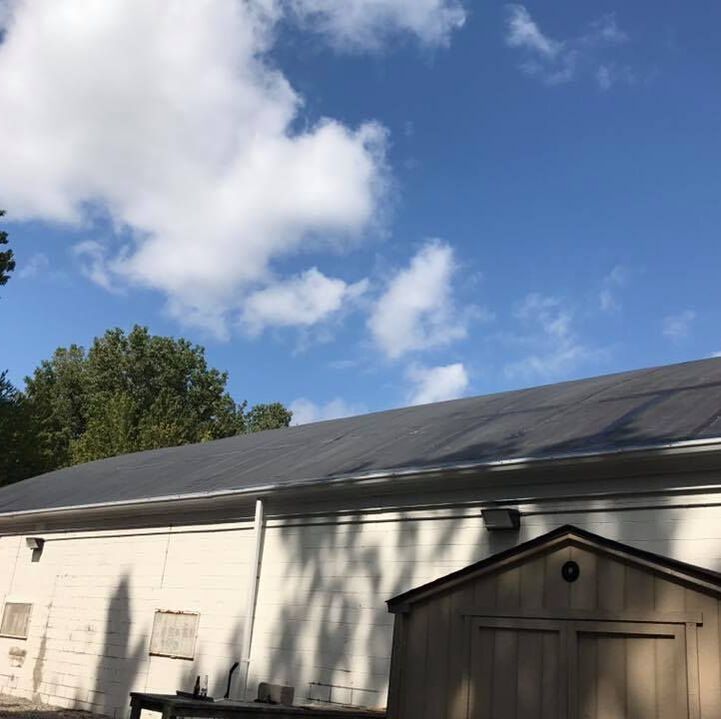 White building with dark roof under a blue sky with fluffy white clouds; small shed in the foreground.