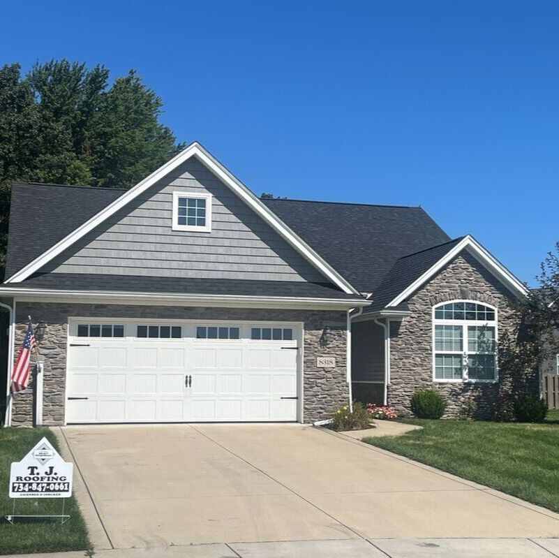 House with gray siding and stone facade, white garage door, and a clear blue sky.