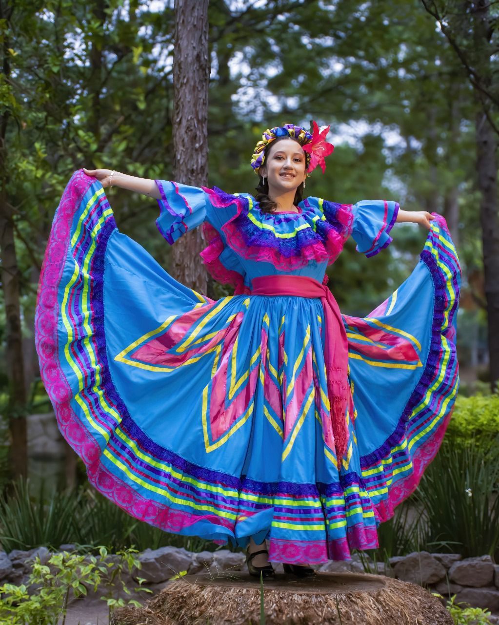 Una mujer con un vestido azul y rosa está parada sobre una roca.