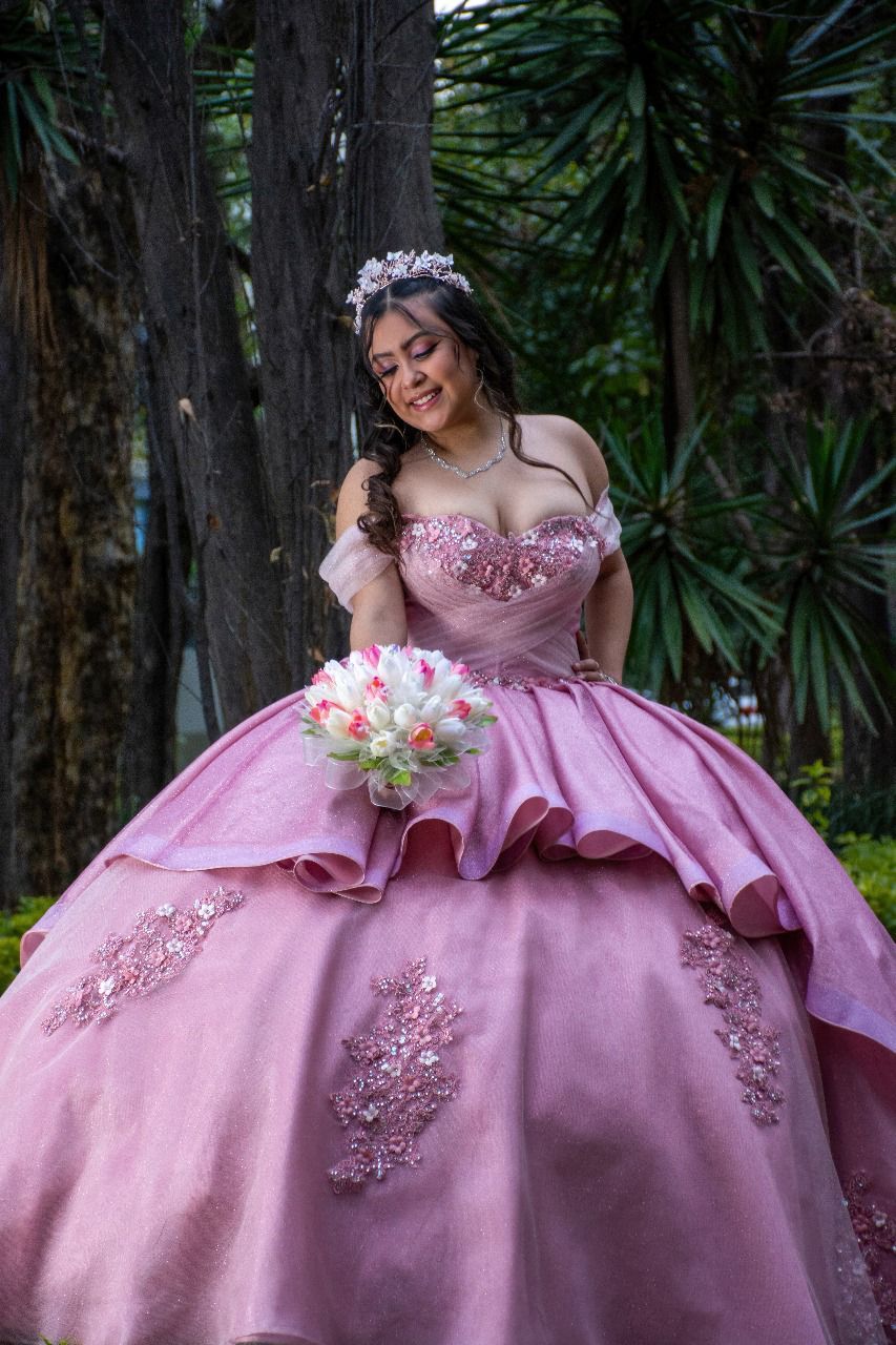 Una mujer con un vestido de fiesta rosa sostiene un ramo de flores.