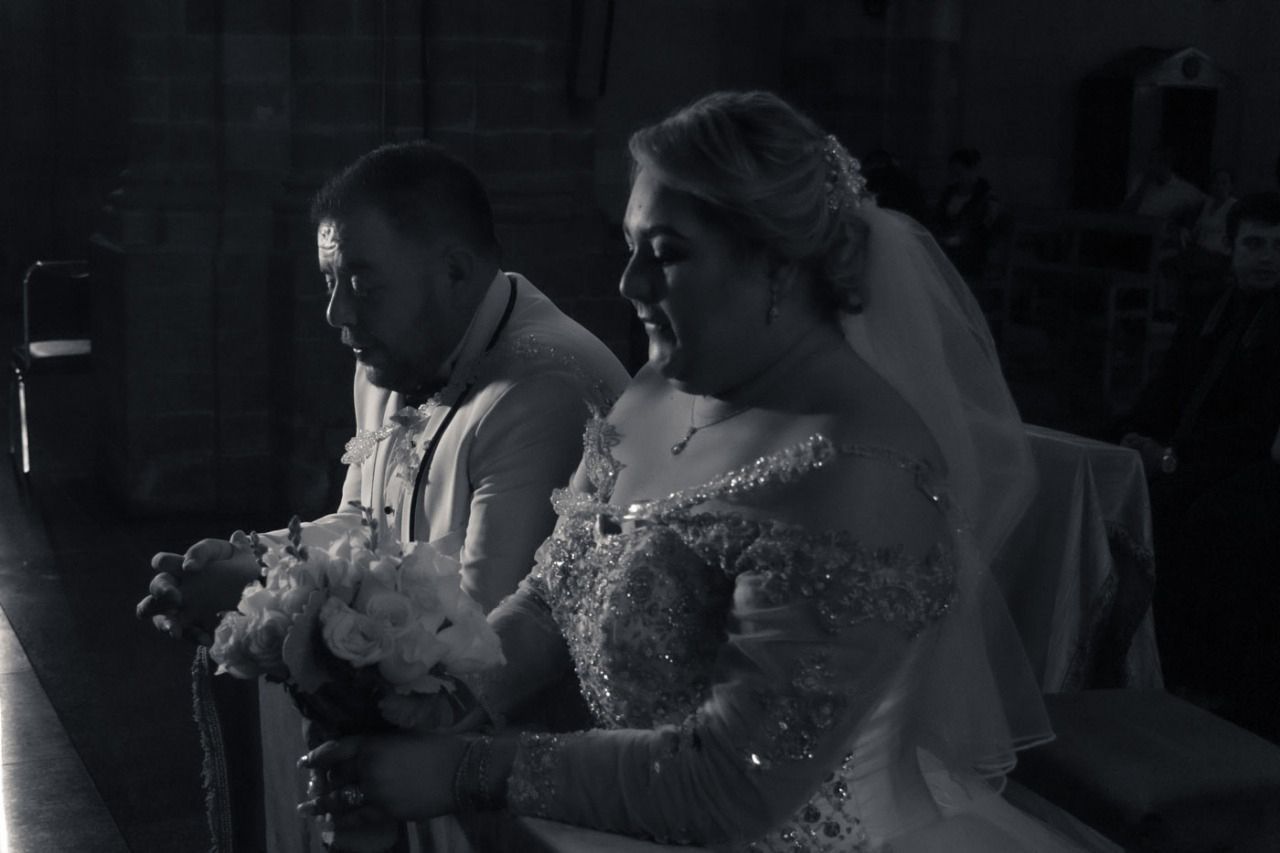 Una novia y un novio están sentados en una iglesia tomados de la mano.