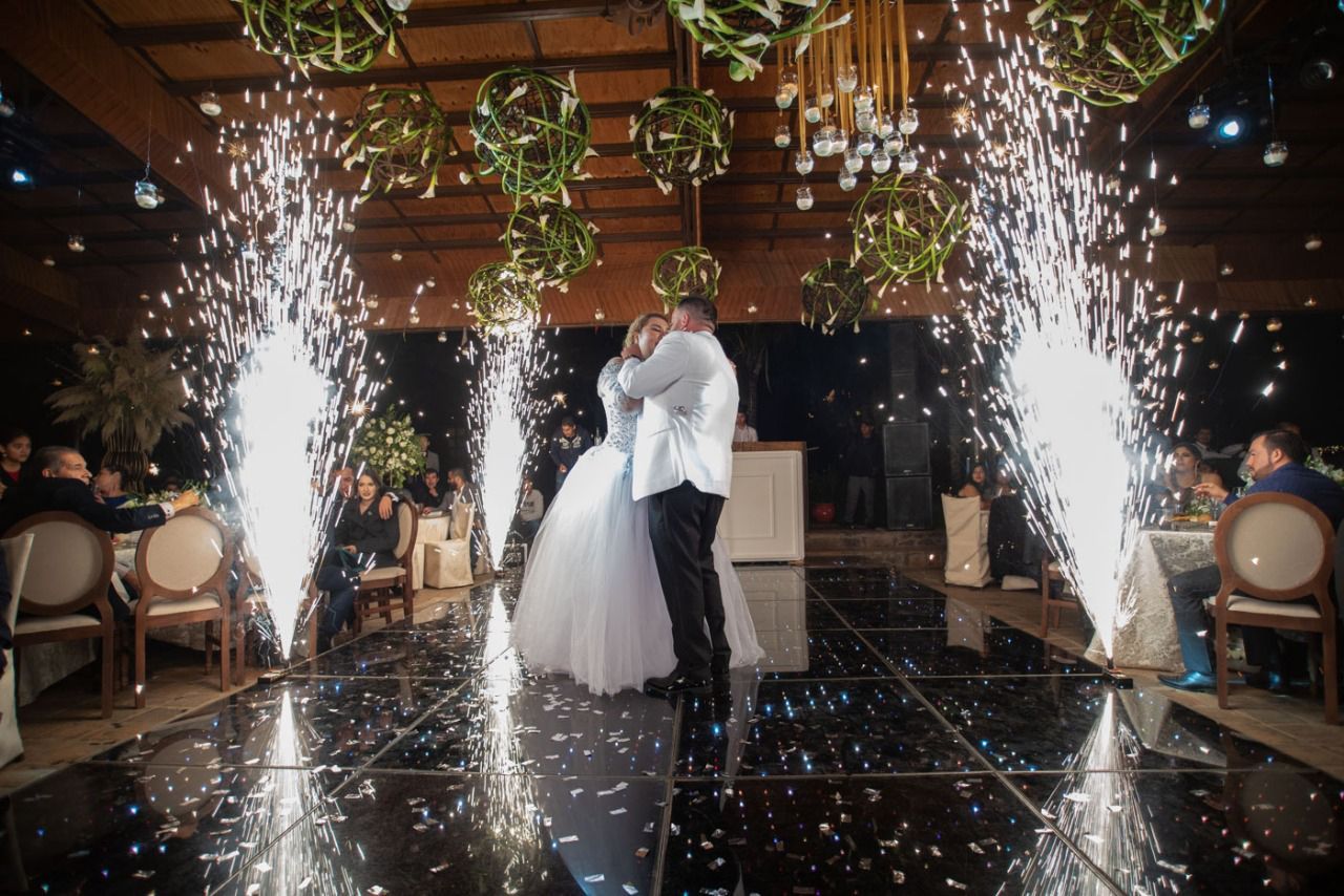 Una novia y un novio están bailando en una pista de baile con bengalas de fondo.