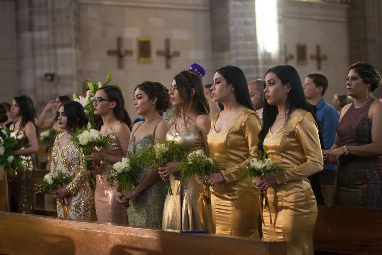 Un grupo de mujeres con vestidos dorados están de pie en una iglesia sosteniendo ramos de flores.