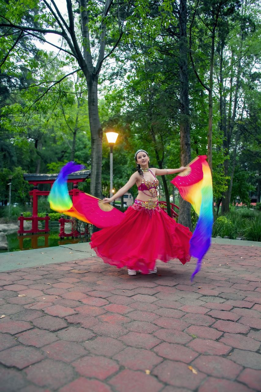 Una mujer con un vestido rojo está bailando con una bandera del arco iris.
