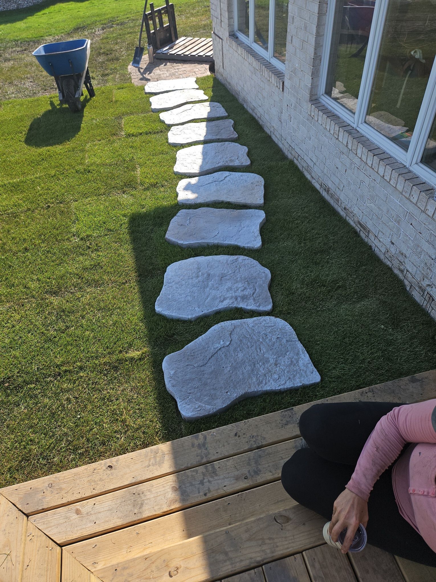 Stepping stones on green grass leading to a house with windows. A person sits nearby.