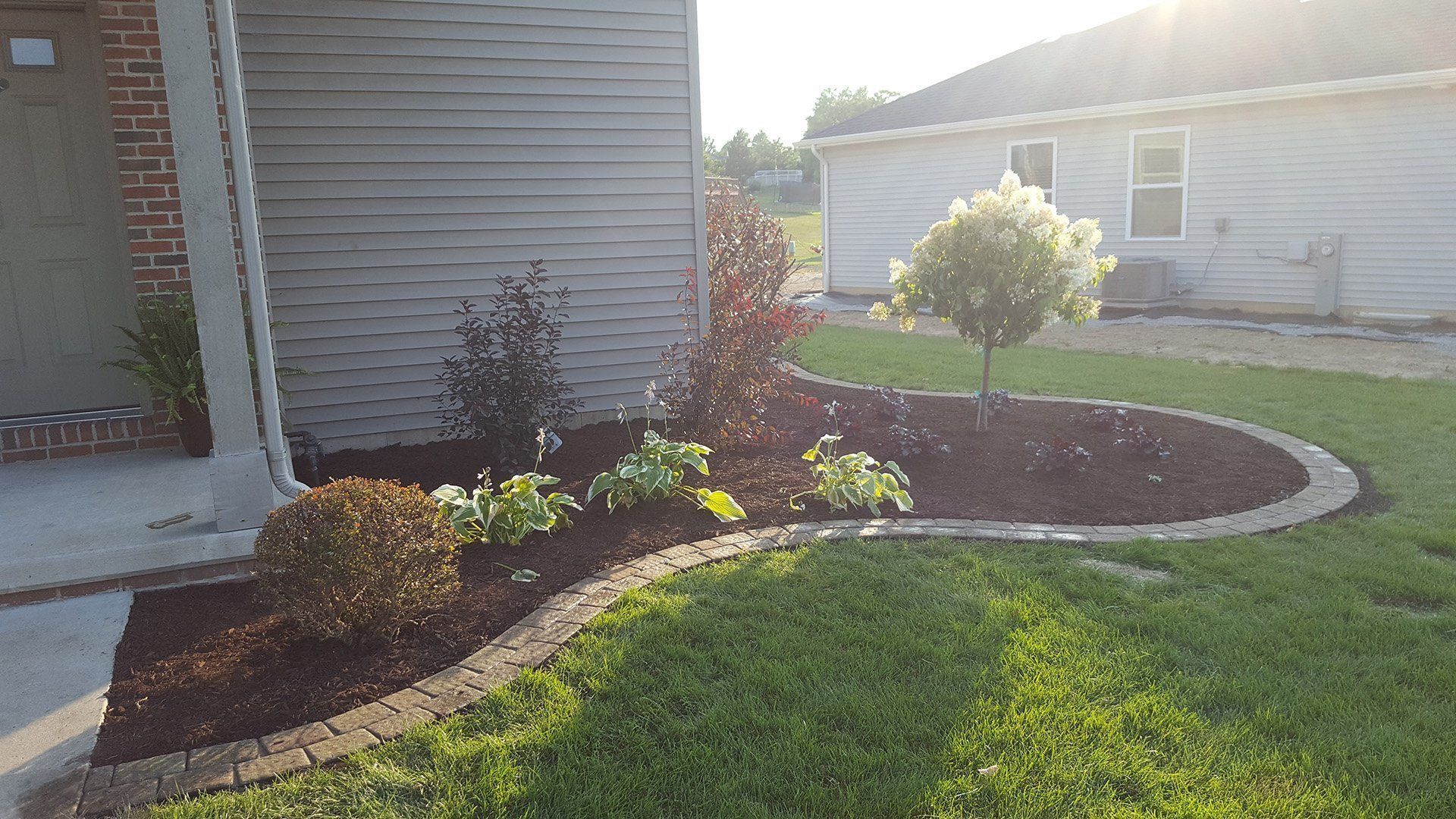 Landscaped front yard with curved flower bed, mulch, and assorted shrubs and a tree.