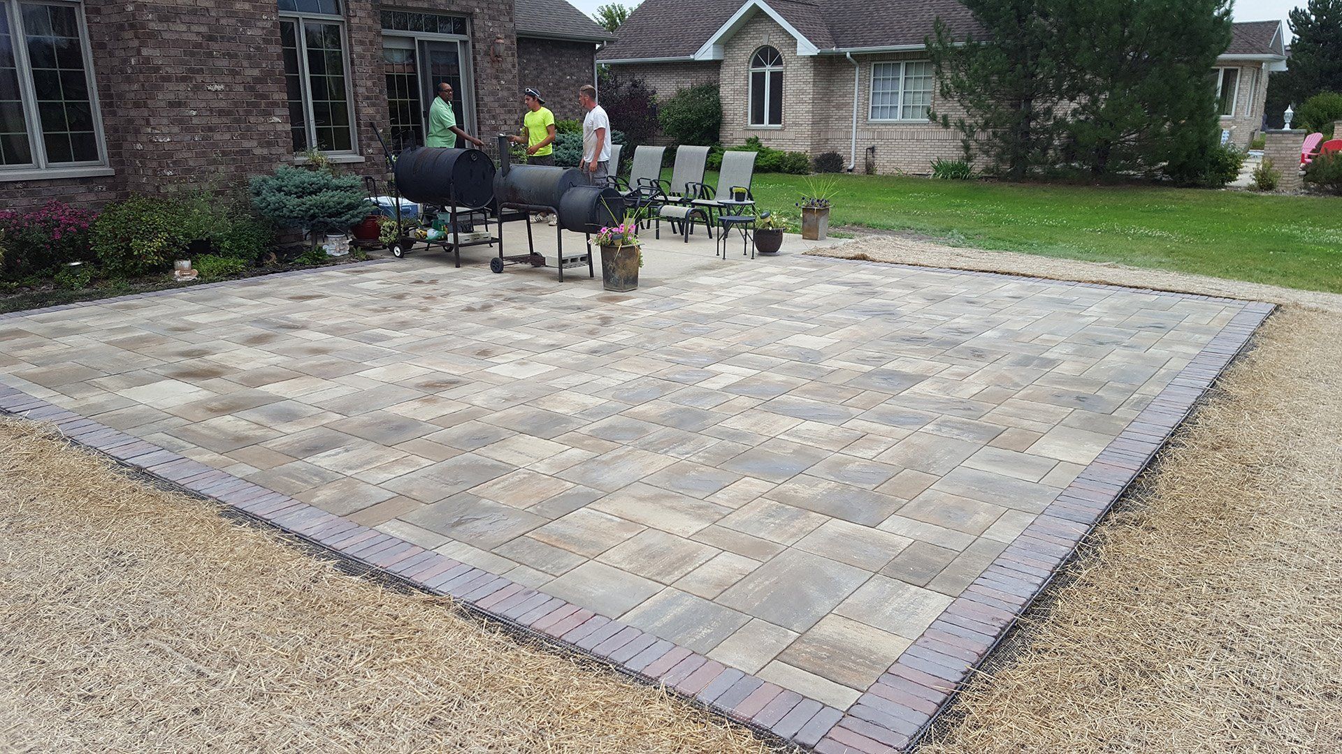 Brick patio with a grill, chairs, and landscaping in a backyard.