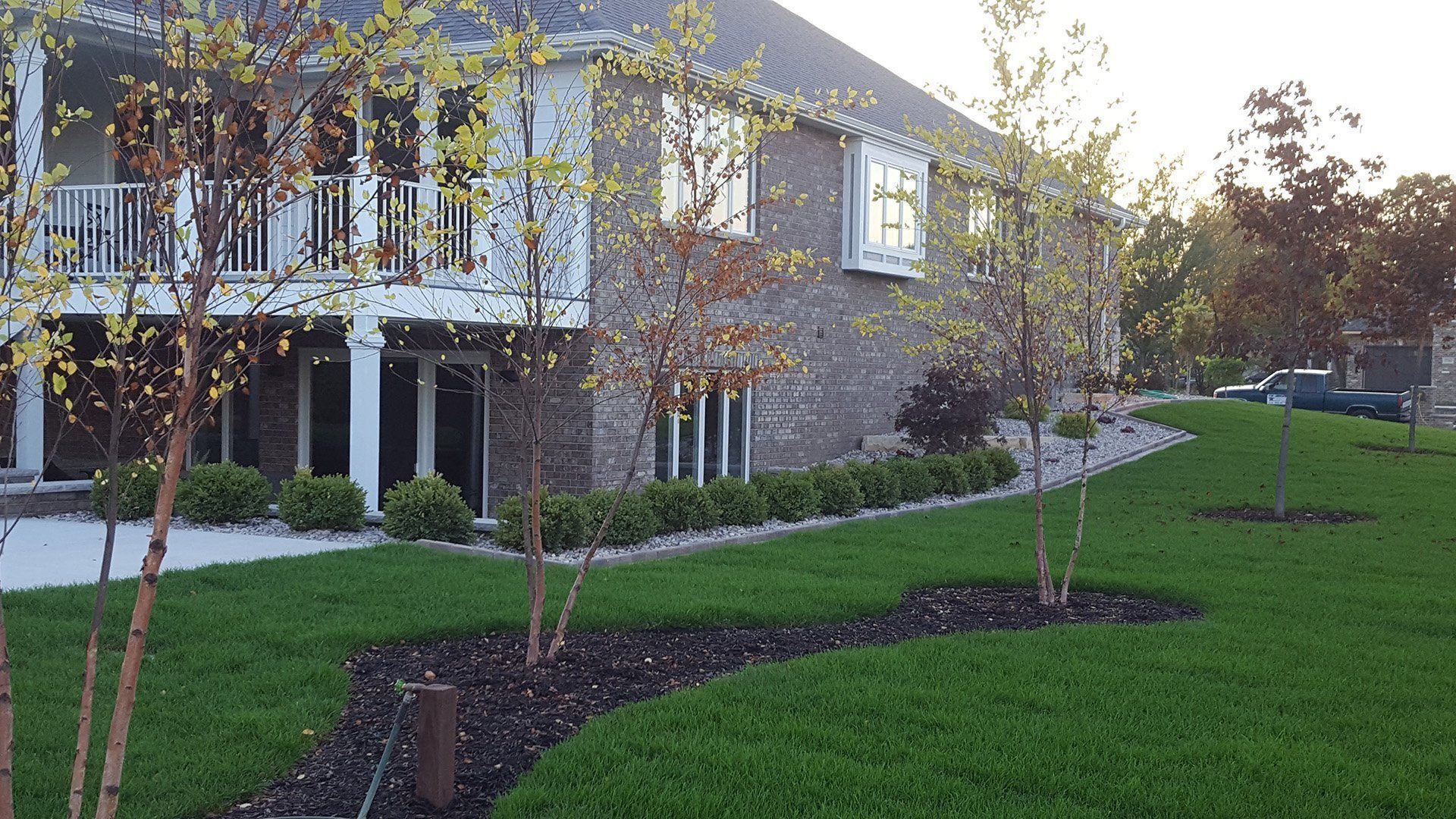 Two-story brick house with a grassy lawn, trees, and landscaping.