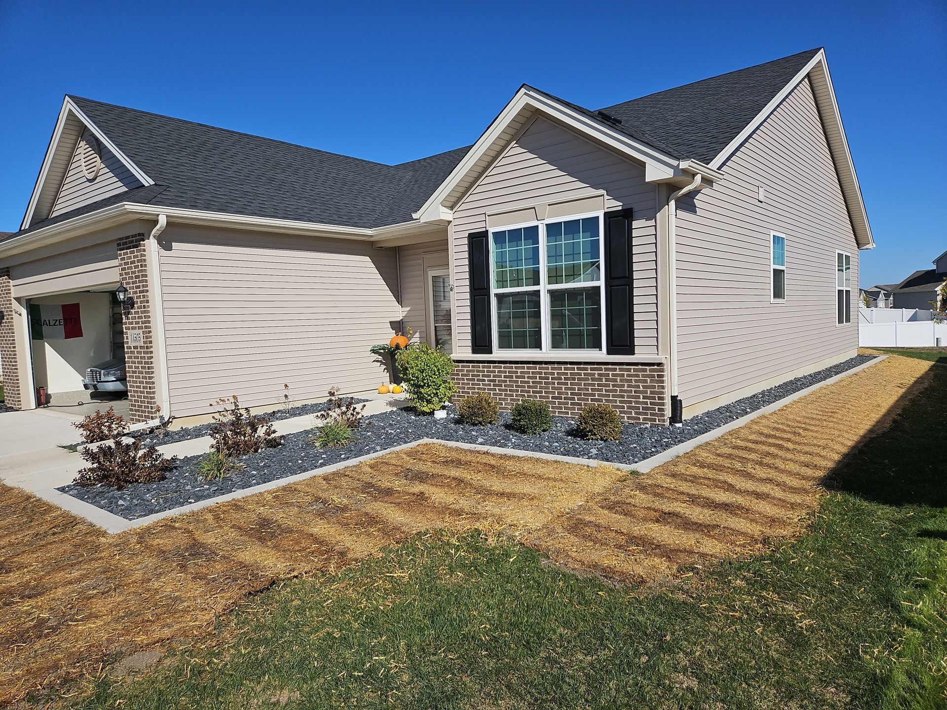 Tan house with black shutters, roof, and rock border, against a blue sky.