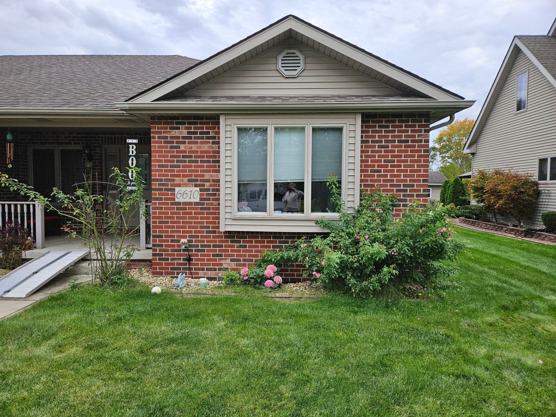 Brick house with a small front yard, ramp for accessibility, and a bay window.