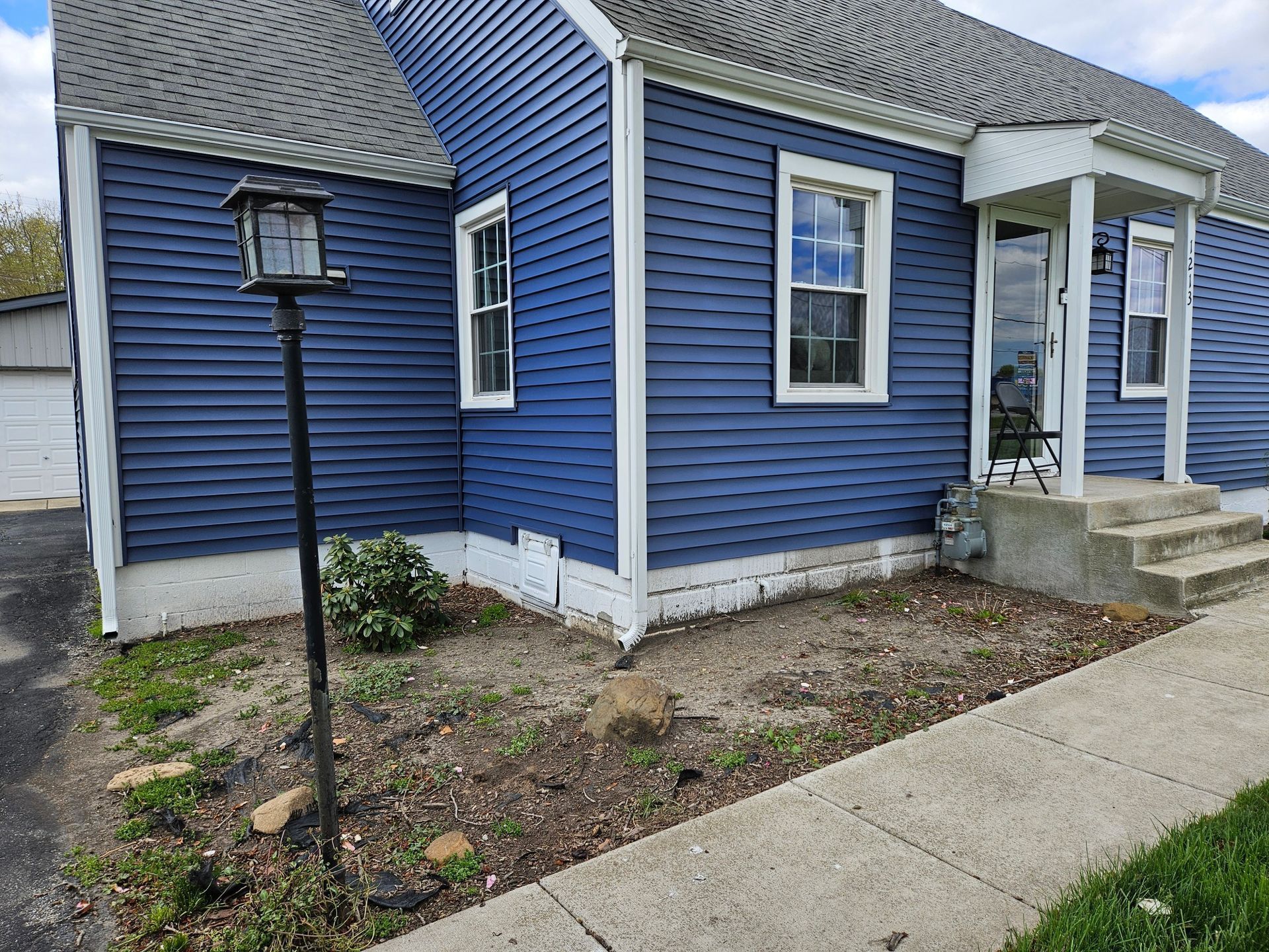 Blue house with white trim, bare dirt landscaping, and bird feeder. Concrete walkway.