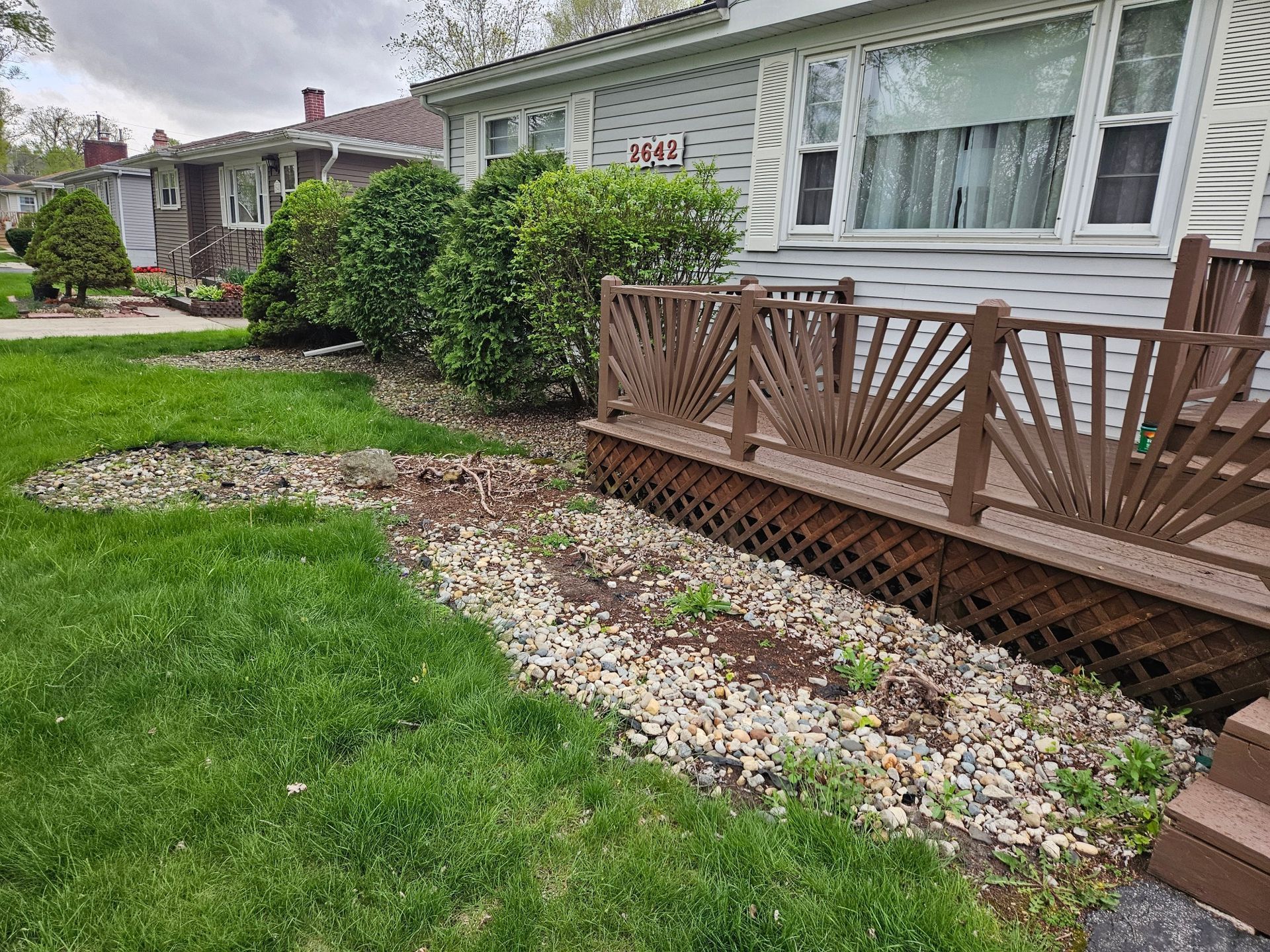 Low-angle view of a house with a wooden deck and gravel-lined landscaping bordering green lawn.