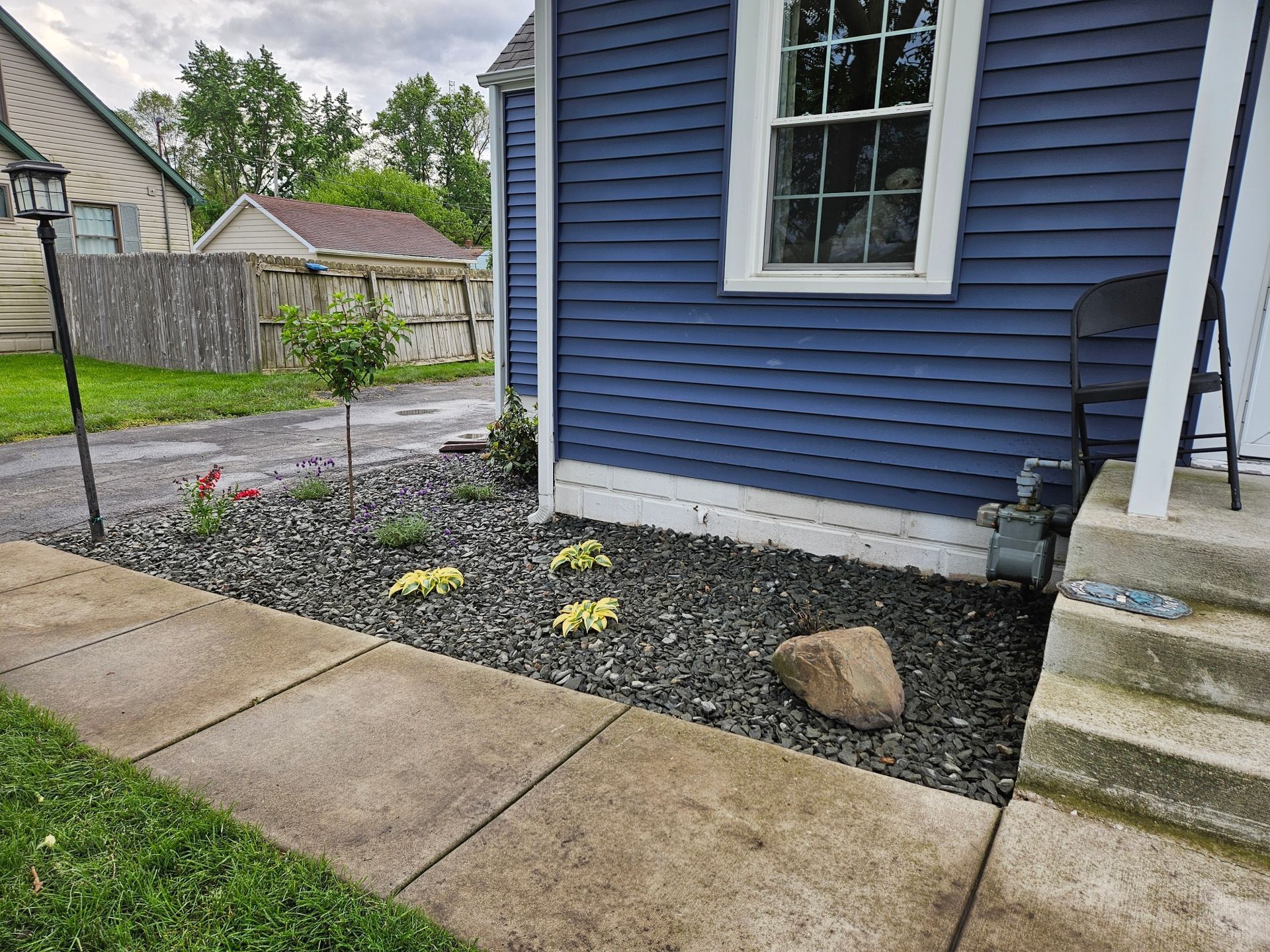 Blue house with garden bed, dark rock mulch, concrete sidewalk.