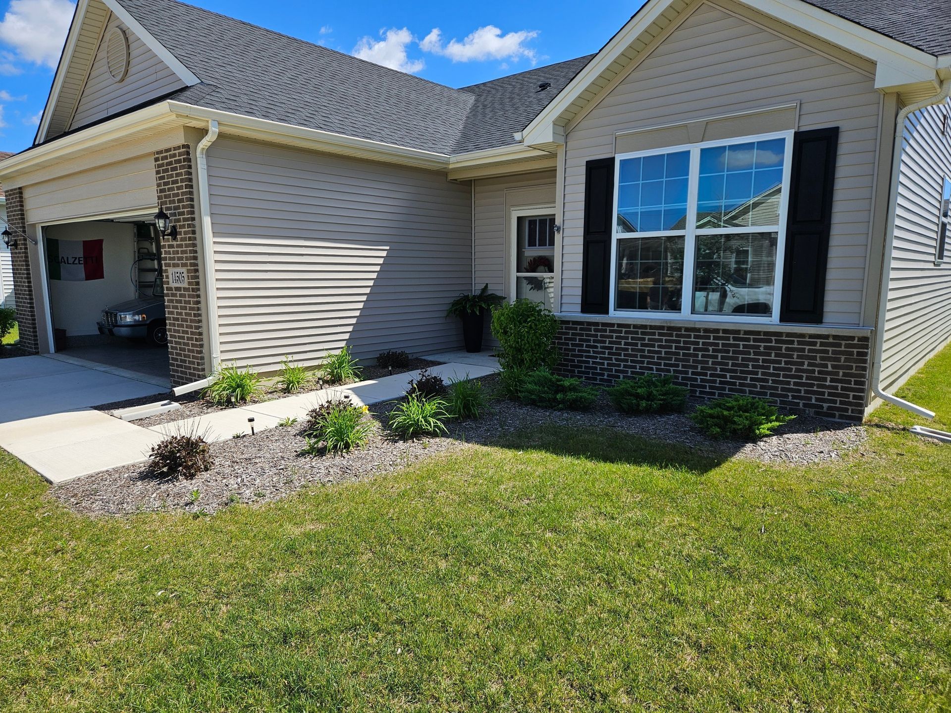 Exterior view of a beige house with a garage and green lawn, blue sky. Small garden with plants.