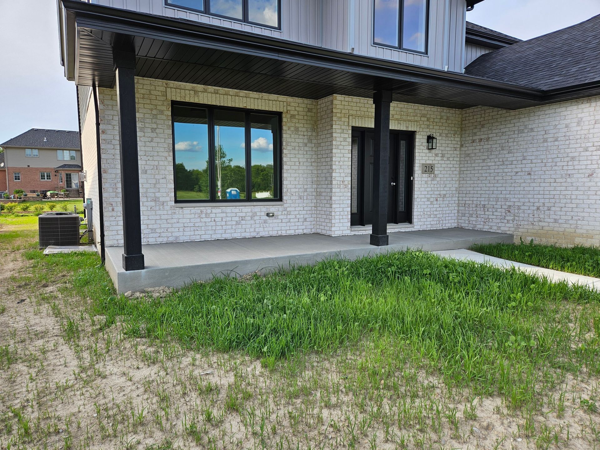 A house with white brick exterior, black trim, and overgrown grass in the yard.