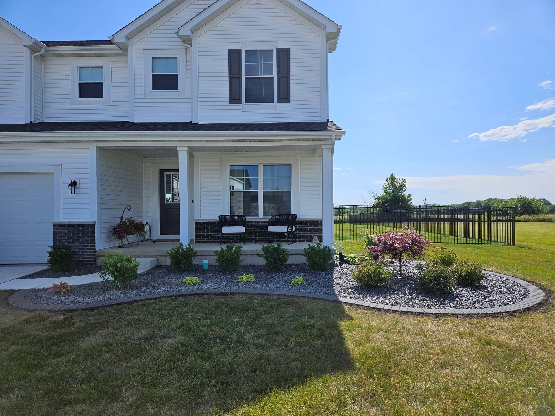White two-story house with front porch and landscaped garden bed with dark rocks and green plants.