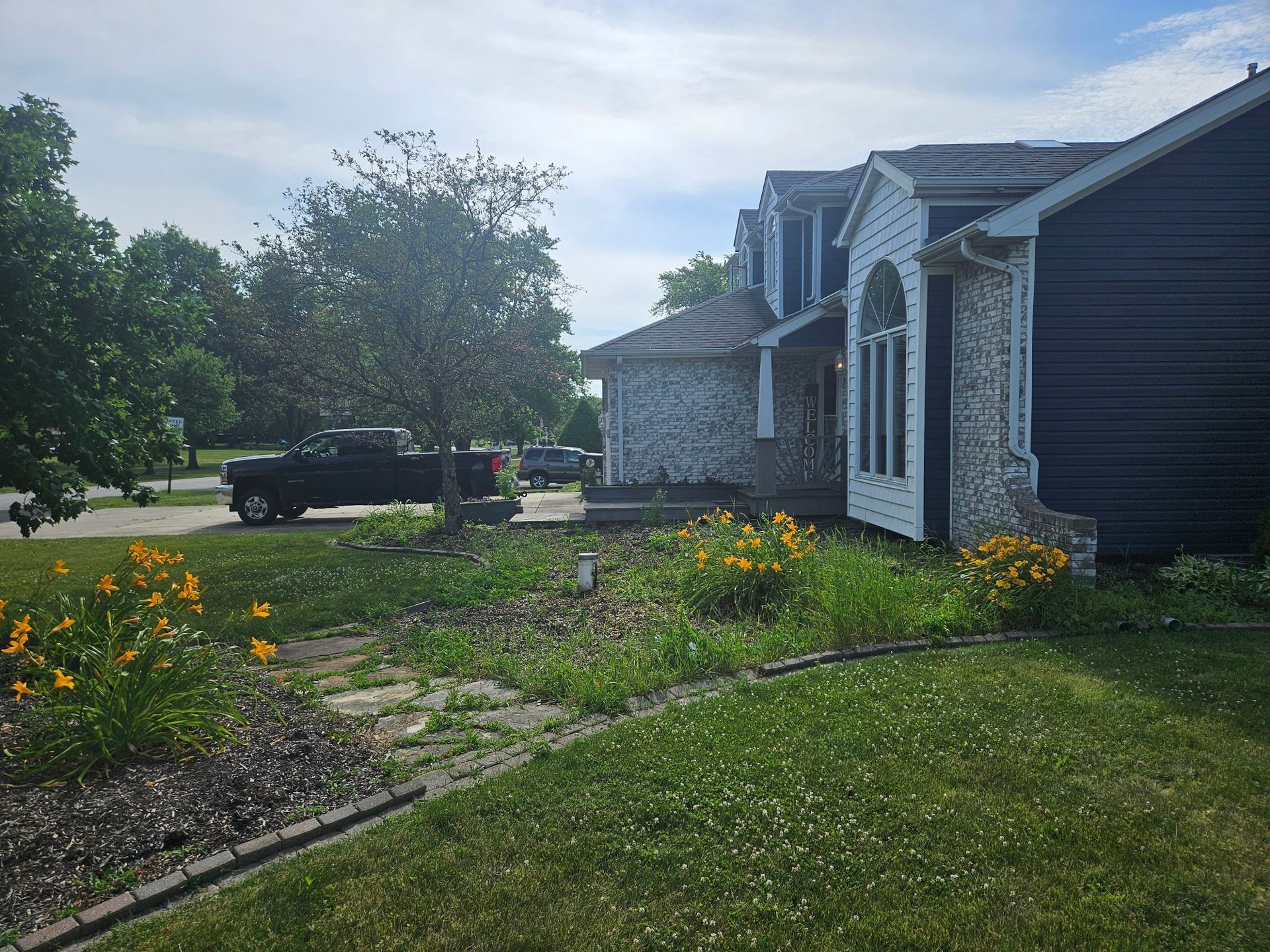 A suburban house with blue siding, stone facade, and a truck parked on the street on a sunny day.