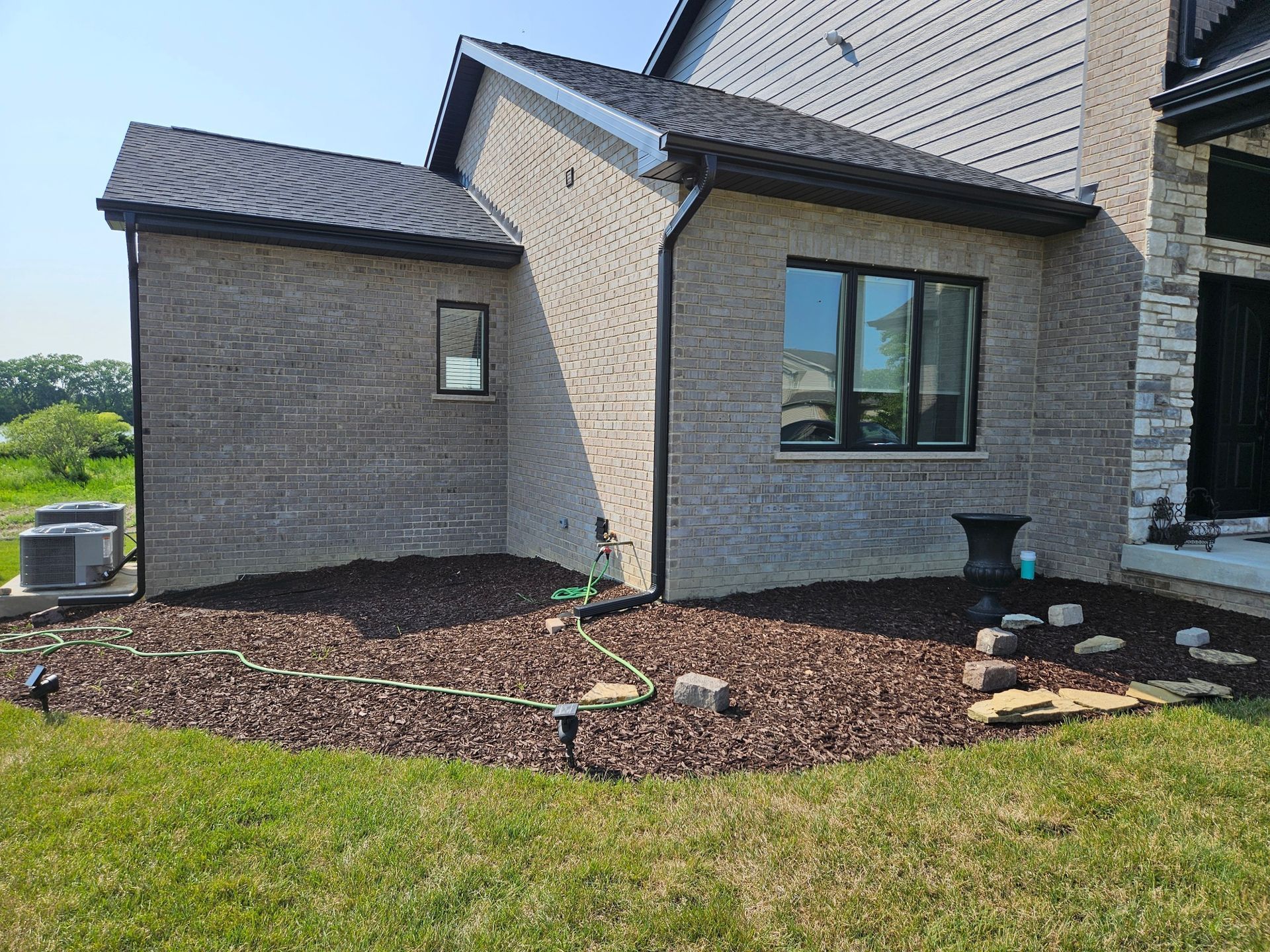 Brick house exterior with dark trim and roof, window, and mulch landscaping.