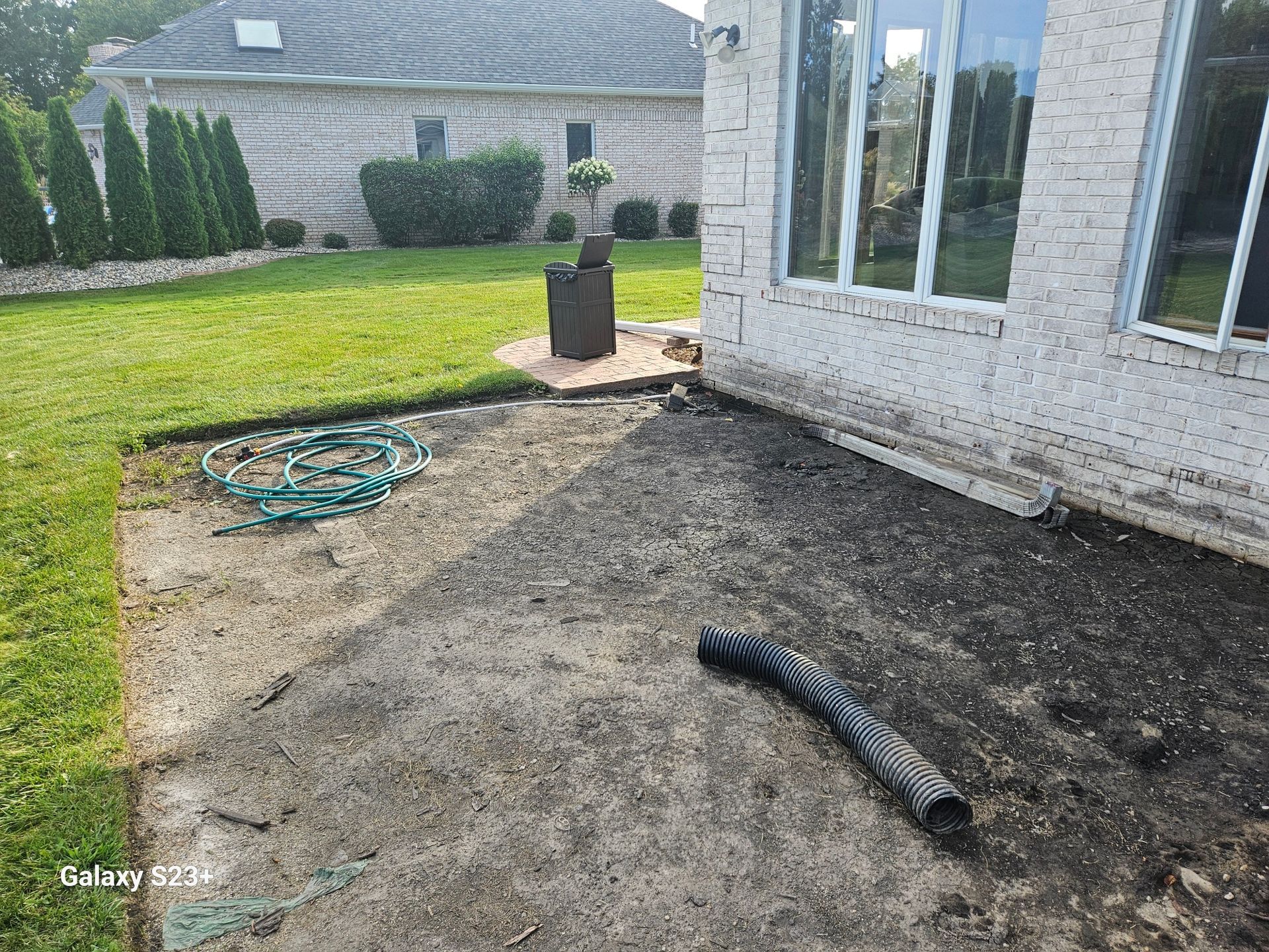 Concrete patio with grass, brick house, and drainage pipe.