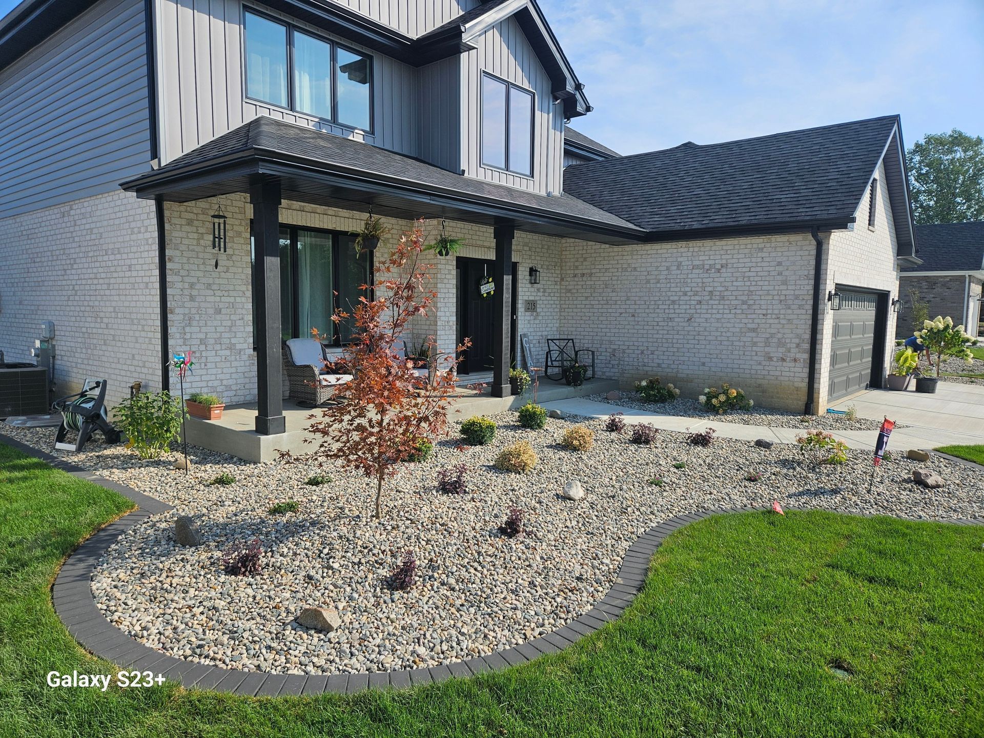Front yard with rock garden, landscaping, and house with black trim and gray siding.