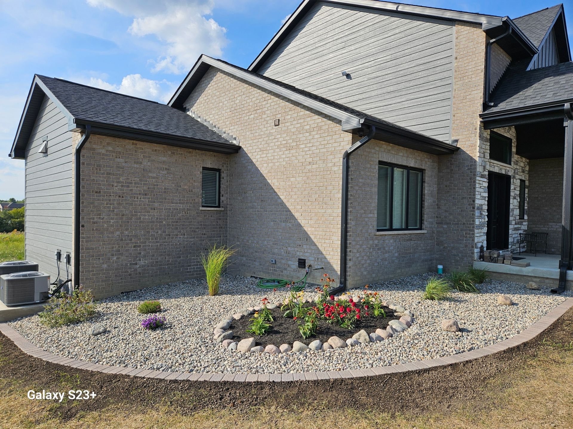Exterior view of a house with brick siding, a flower bed with red flowers, and gray gravel.