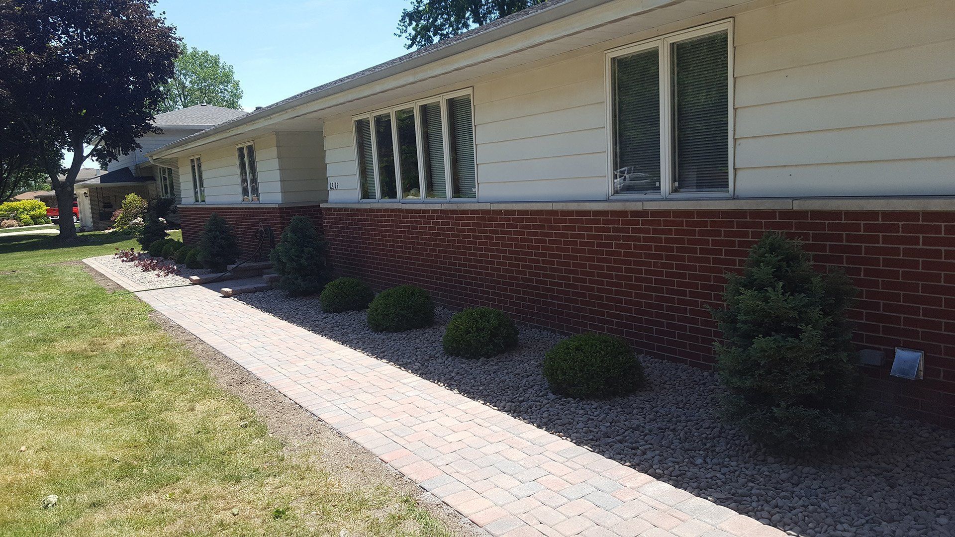 Brick-faced house with windows, landscaping, a stone walkway, and lawn on a sunny day.
