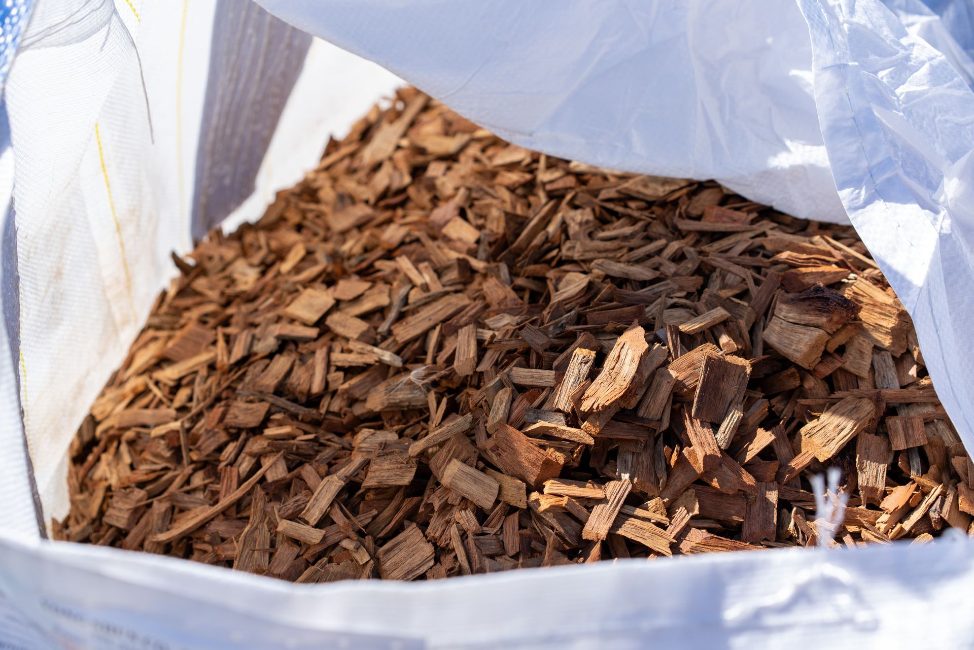 Brown wood chips mulch in large white bulk bag close-up view outdoors in sunlight. Brown wood chips mulch in large white bulk bag close-up view outdoors in sunlight.
