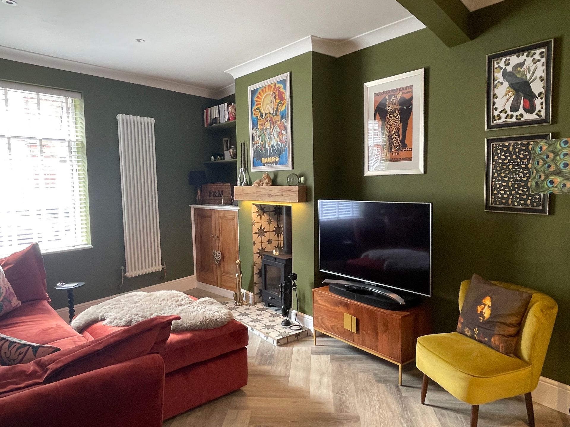 A living room with green walls , a red couch , a yellow chair and a flat screen tv.