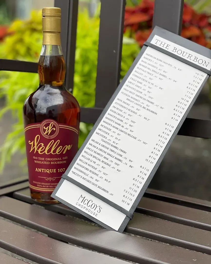 A bottle of weller whiskey is sitting on a wooden bench next to a menu.
