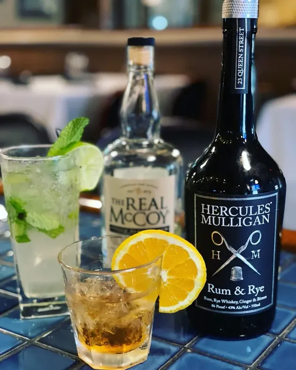 A bottle of hercules mulligan rum and rye next to a drink
