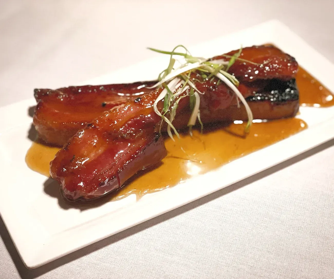 A white plate topped with meat and sauce on a table