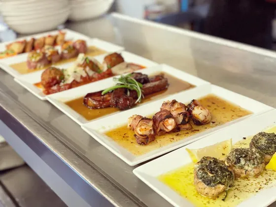 A row of white plates filled with different types of food on a counter.