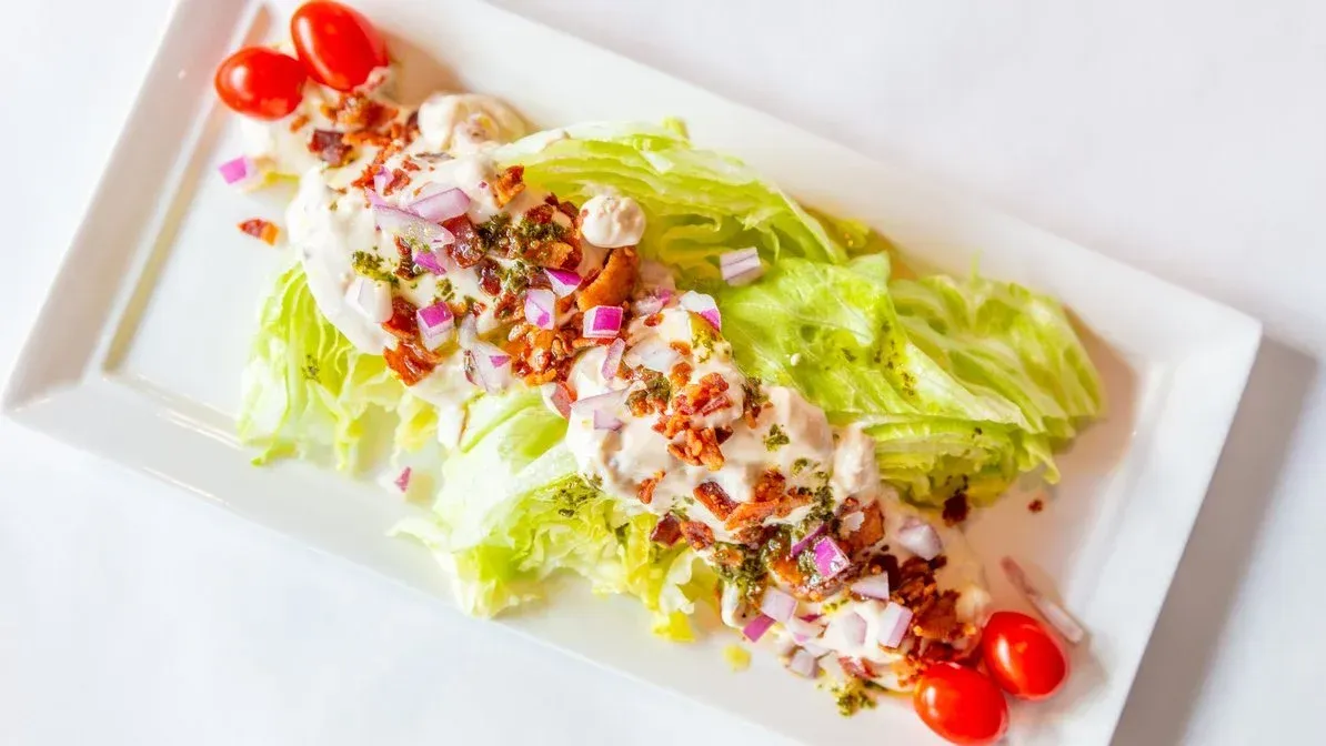 A white plate topped with lettuce , tomatoes and bacon.