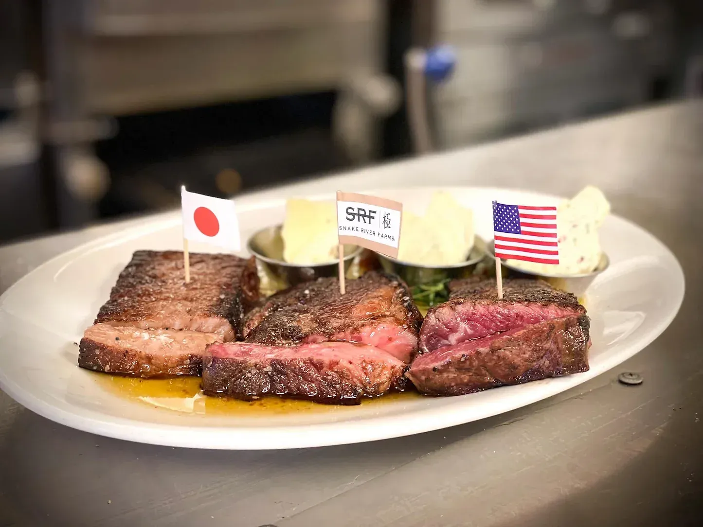 A white plate topped with steaks , butter , and flags.