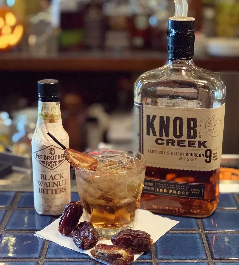 A bottle of knob creek whiskey next to a glass of whiskey and dates.