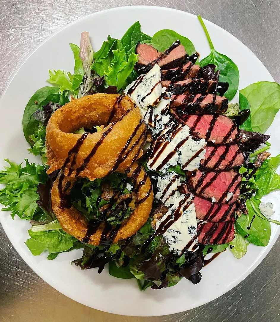 A white plate topped with steak , onion rings , and spinach.