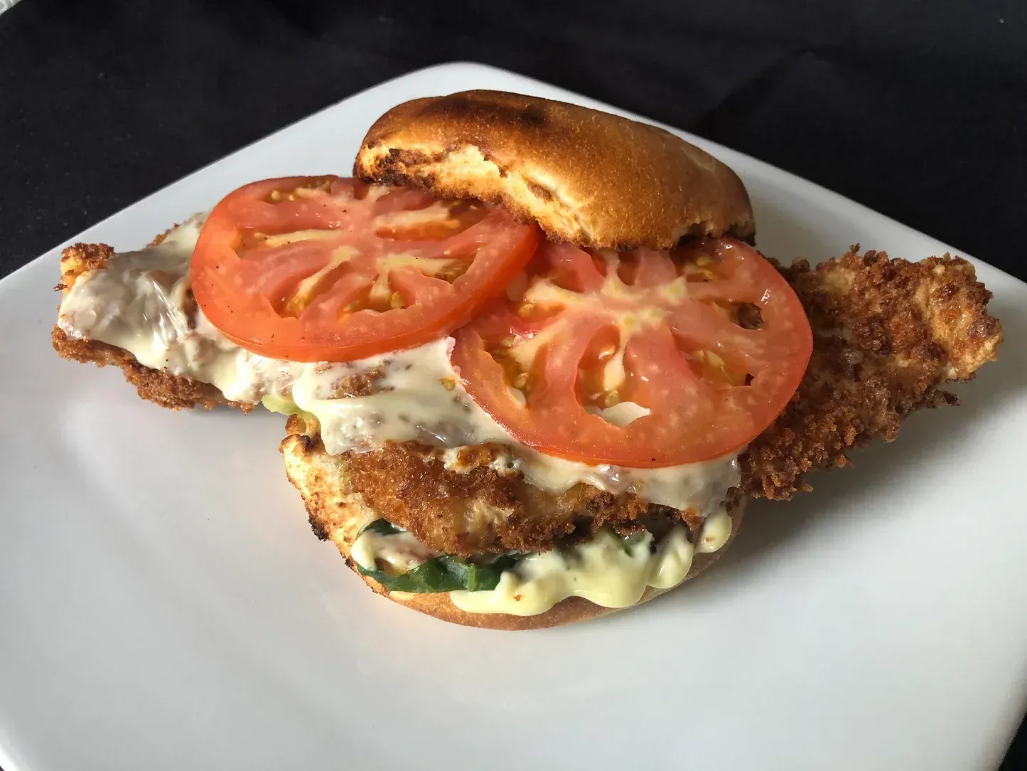 A chicken sandwich with tomatoes and mayonnaise on a white plate