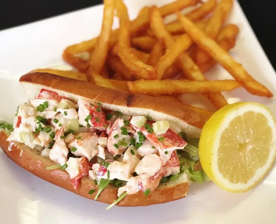 A lobster roll and french fries on a white plate